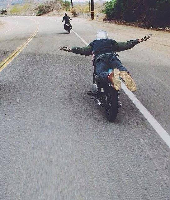 A rider in superman pose on a moving motorcycle on an open canyon road