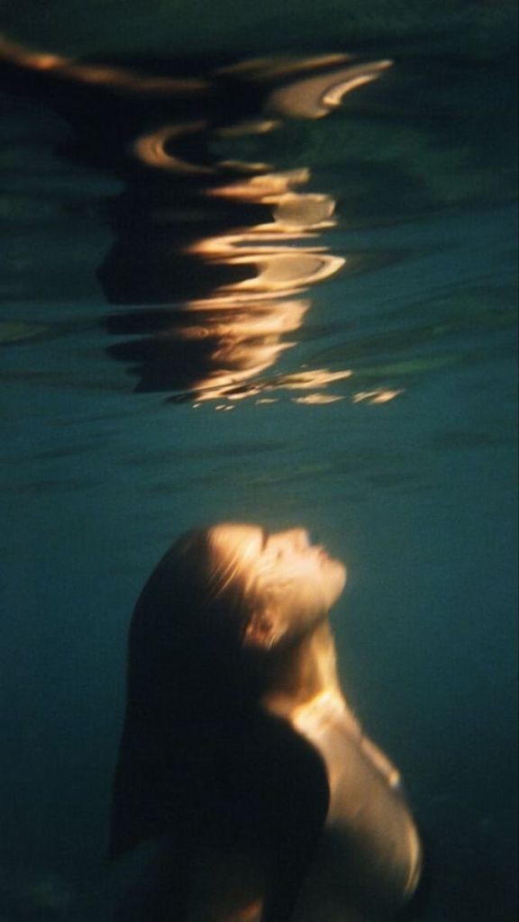 A woman underwater rising toward golden surface light