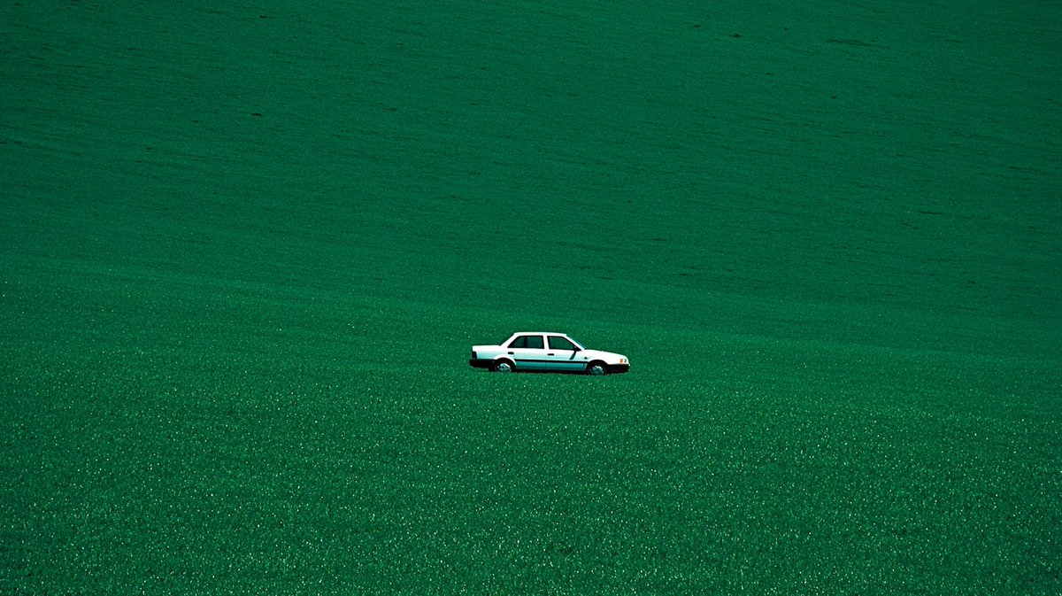 A white sedan alone in an endless green field